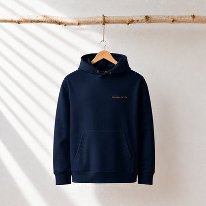 Sweat à capuche bio bleu marine avec inscription 'Massage is life', suspendu à une branche en bois