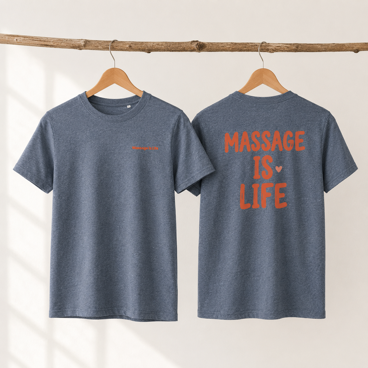 T-shirt bio gris avec inscription 'Massage Is Life' en orange, suspendu sur cintre en bois