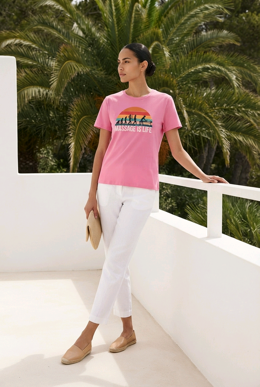 T-shirt rose bio Massage Is Life avec imprimé coucher de soleil, porté avec pantalon blanc et espadrilles, fond palmiers